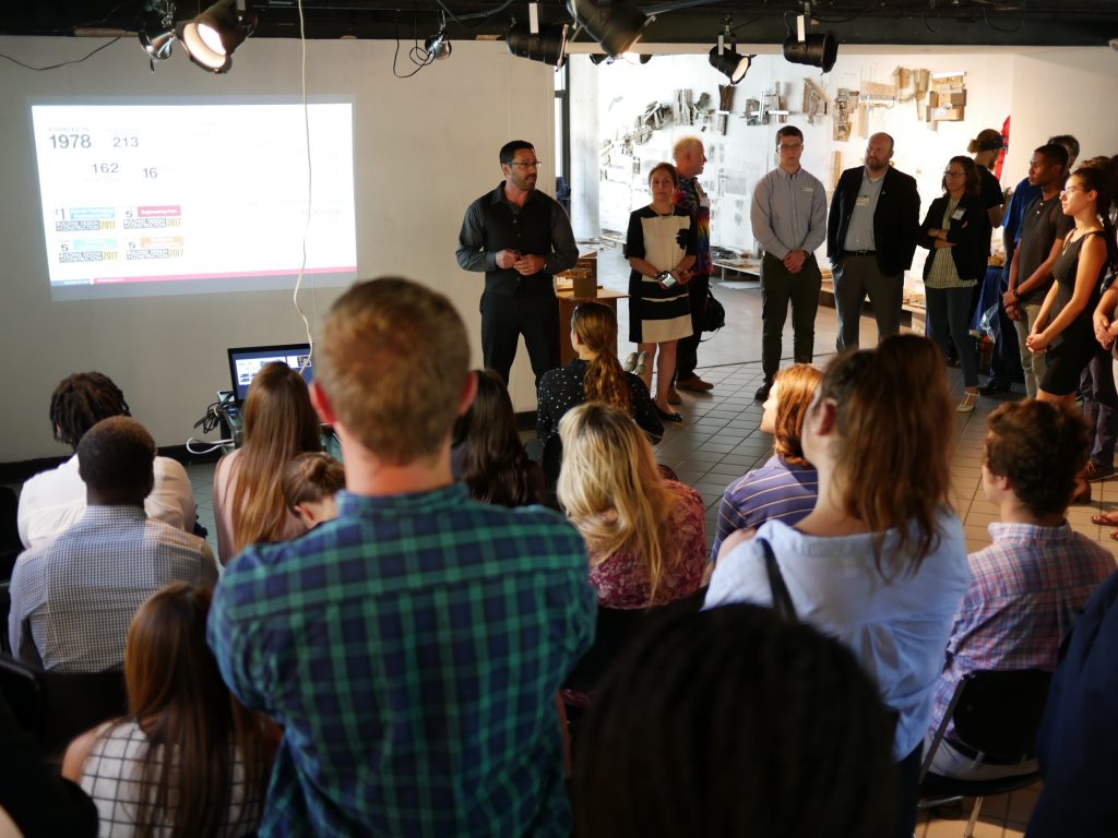 A keynote speaker stands by a projection screen in front of an audience.