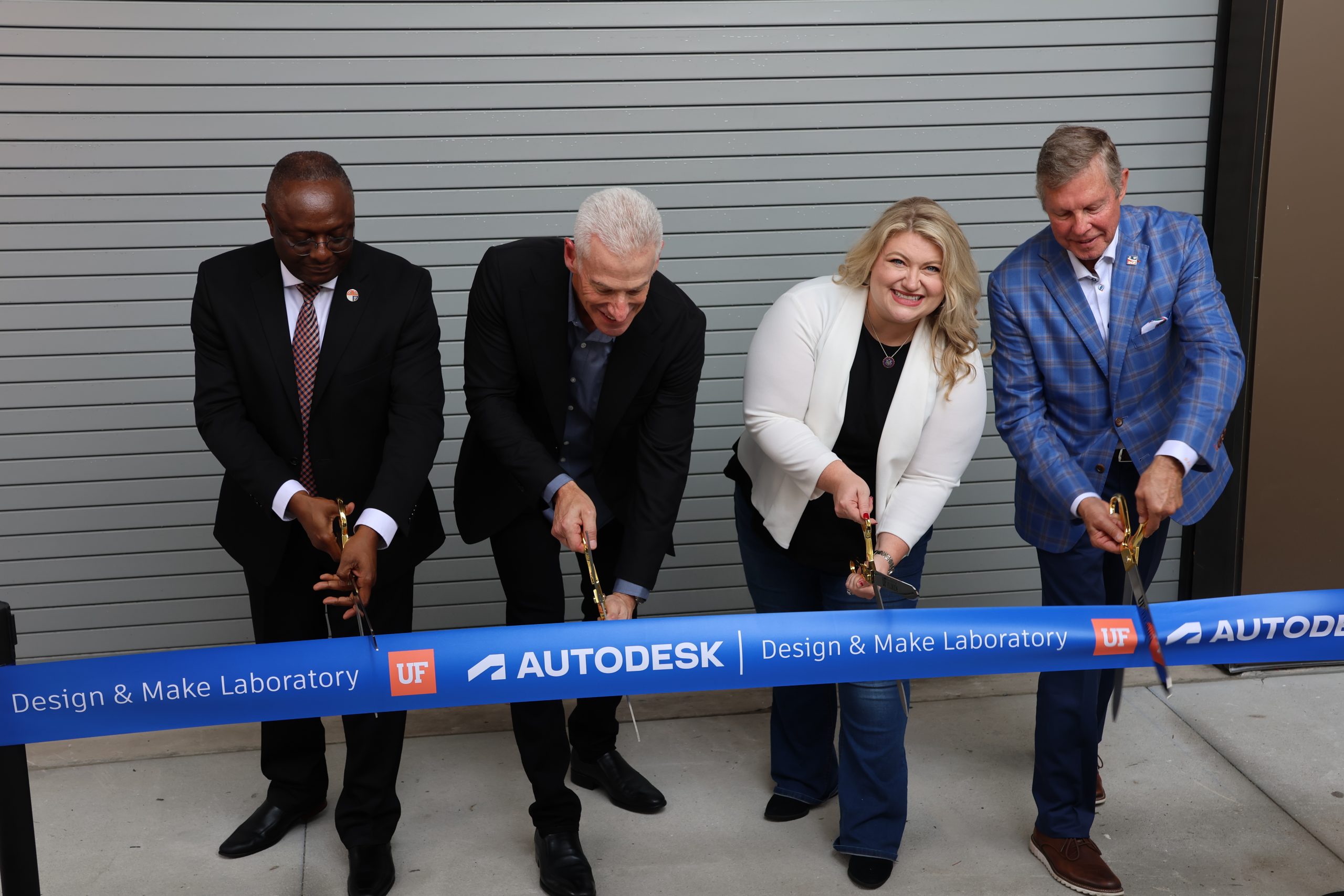 Four people cut a blue ribbon that reads Autodesk Design & Make Laboratory UF at an opening ceremony in front of a gray metal door.